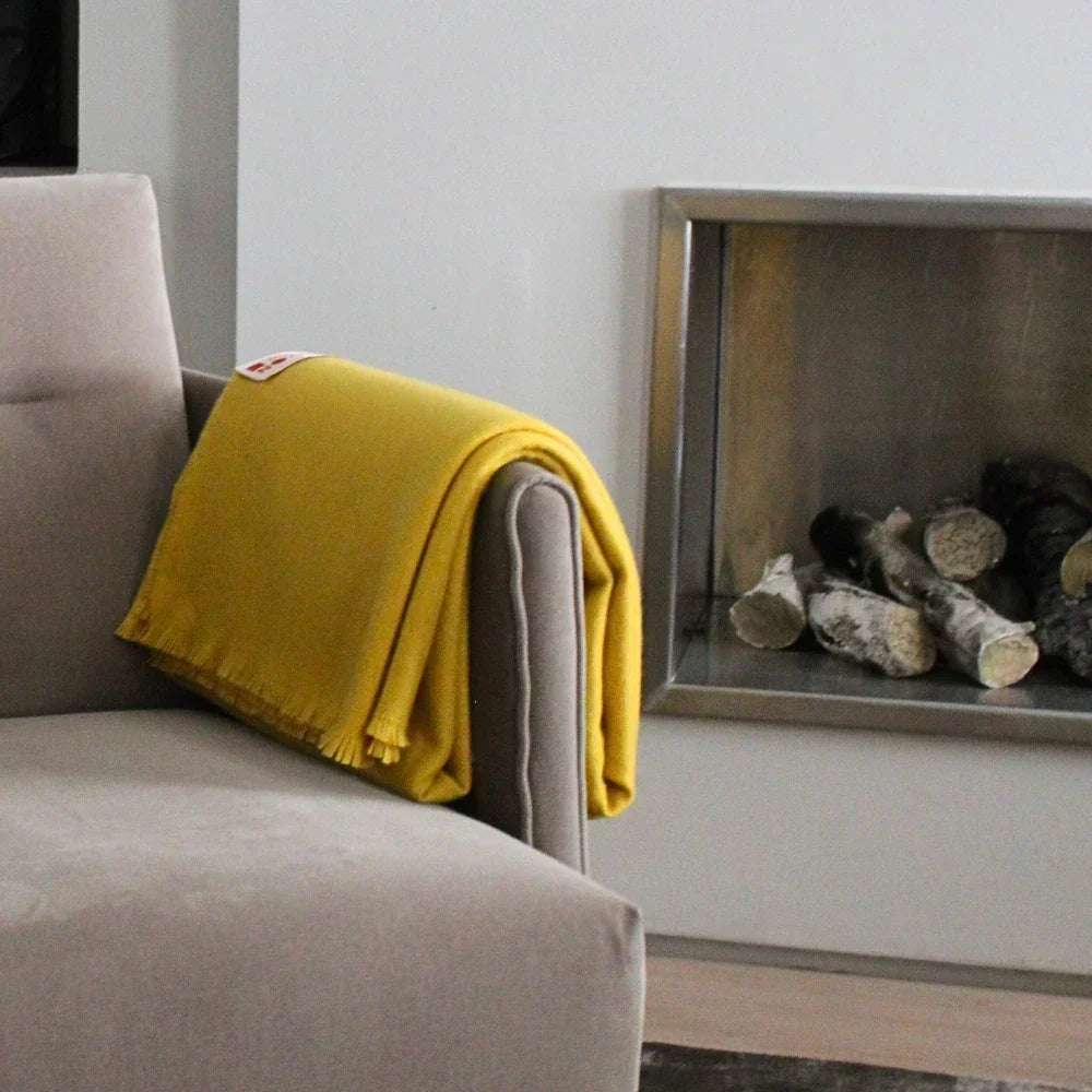Mustard yellow wool throw draped over a neutral armchair beside a contemporary fireplace.
