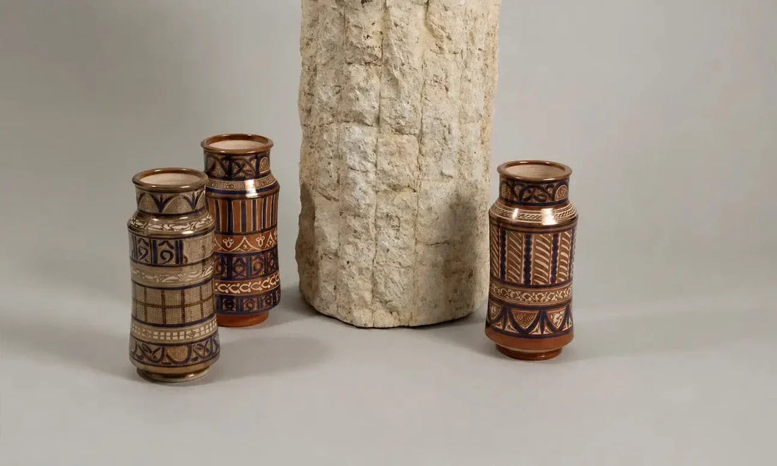 Three hand-painted lustreware ceramic vases with geometric patterns in warm metallic tones and deep blue, arranged around a textured stone plinth.
