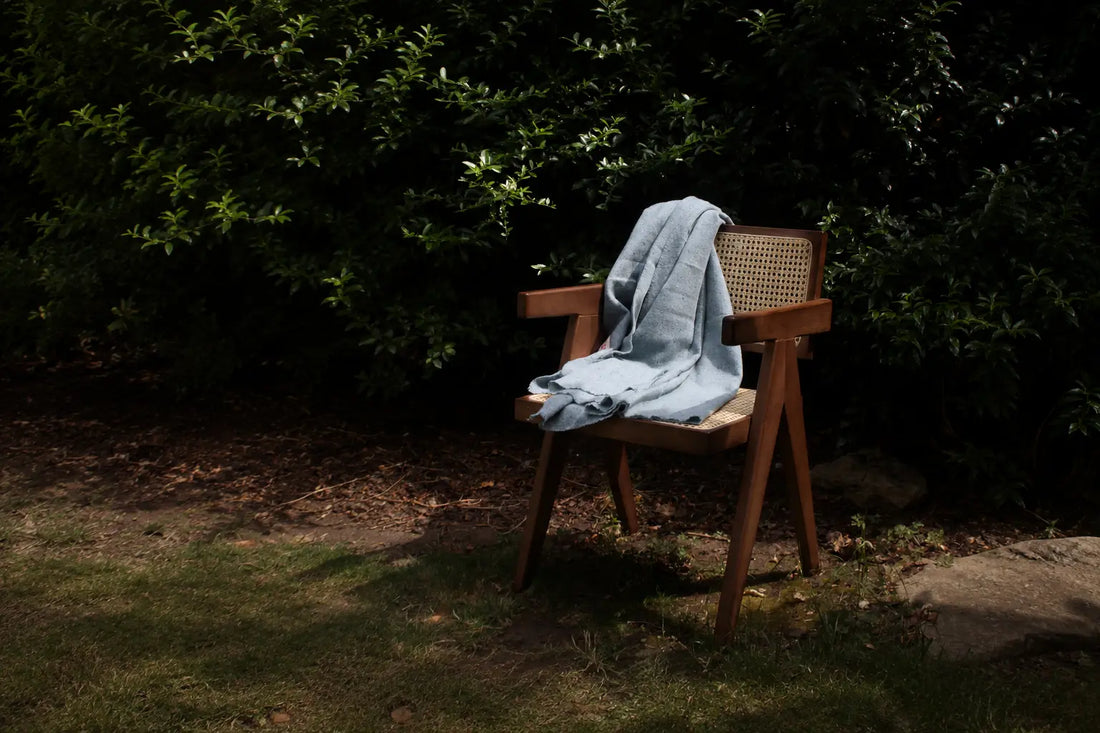 Light denim blue wool throw draped over a wooden cane chair in a sunlit garden.