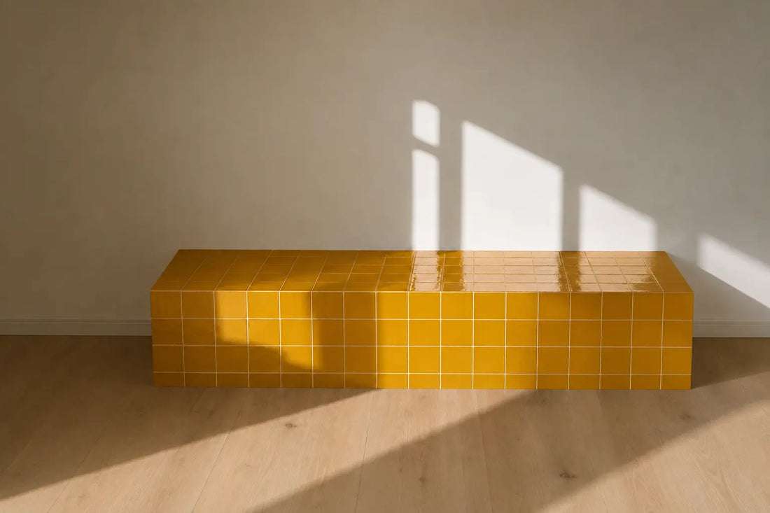 Saffron yellow gloss ceramic tiles covering a tiled bench, illuminated by warm natural sunlight against a neutral wall and wooden floor.