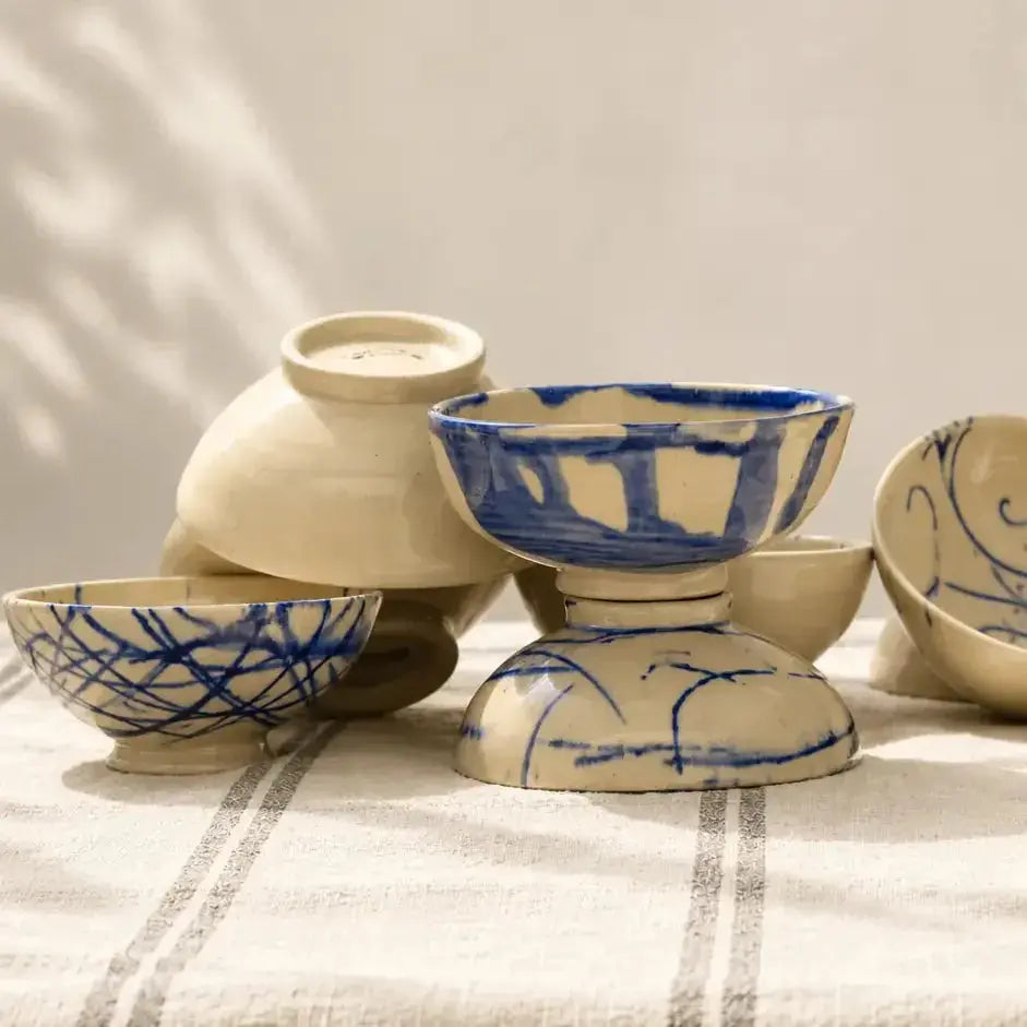 Hand-painted ceramic bowls and vase in cobalt blue and cream, arranged on a natural linen cloth in warm sunlight.