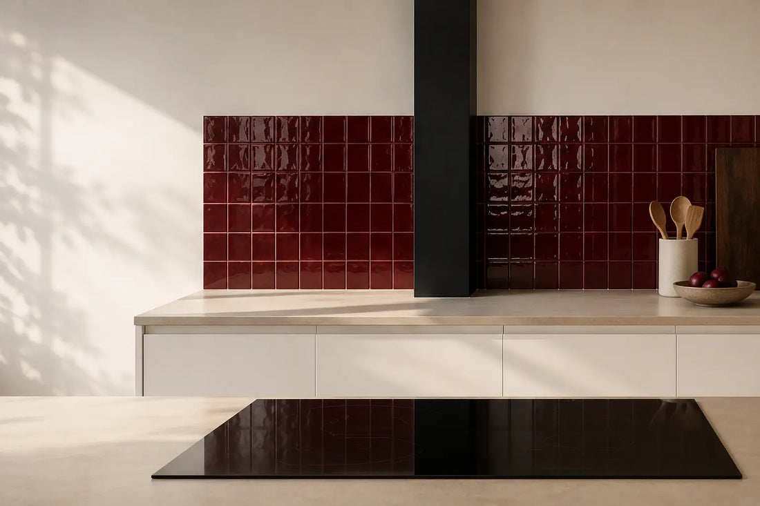 Wine red gloss ceramic tiles used as a kitchen backsplash, paired with cream cabinetry and a black extractor hood in warm natural light.