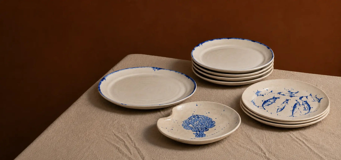 Hand-painted ceramic plates in cream and cobalt blue arranged on a natural linen tablecloth.