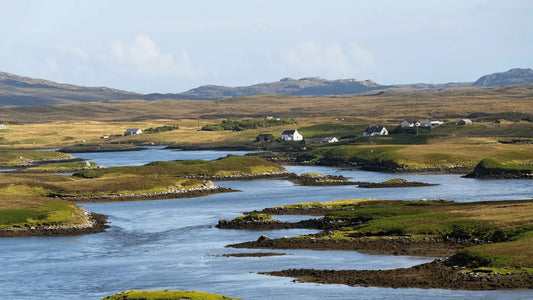 A serene Scottish landscape with rolling hills, scattered cottages, and winding waterways, reflecting the natural beauty that inspires our cashmere and wool throws, woven with care in Scotland.