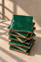 A stack of glossy emerald dark green square coasters on a textured beige surface against a matching beige wall.