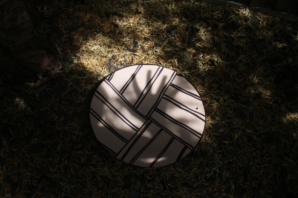 A decorative ceramic plate on the ground with a tree shadows cast over it.