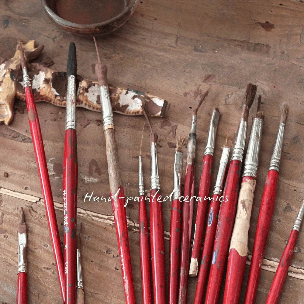 A set of worn red-handled paintbrushes laid out on a wooden surface.