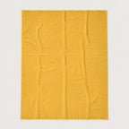 A rectangular mustard yellow throw blanket with fringed edges, laid flat against a light gray background.