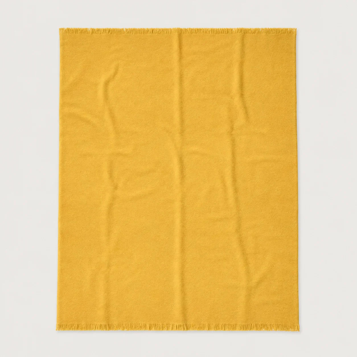 A rectangular mustard yellow throw blanket with fringed edges, laid flat against a light gray background.