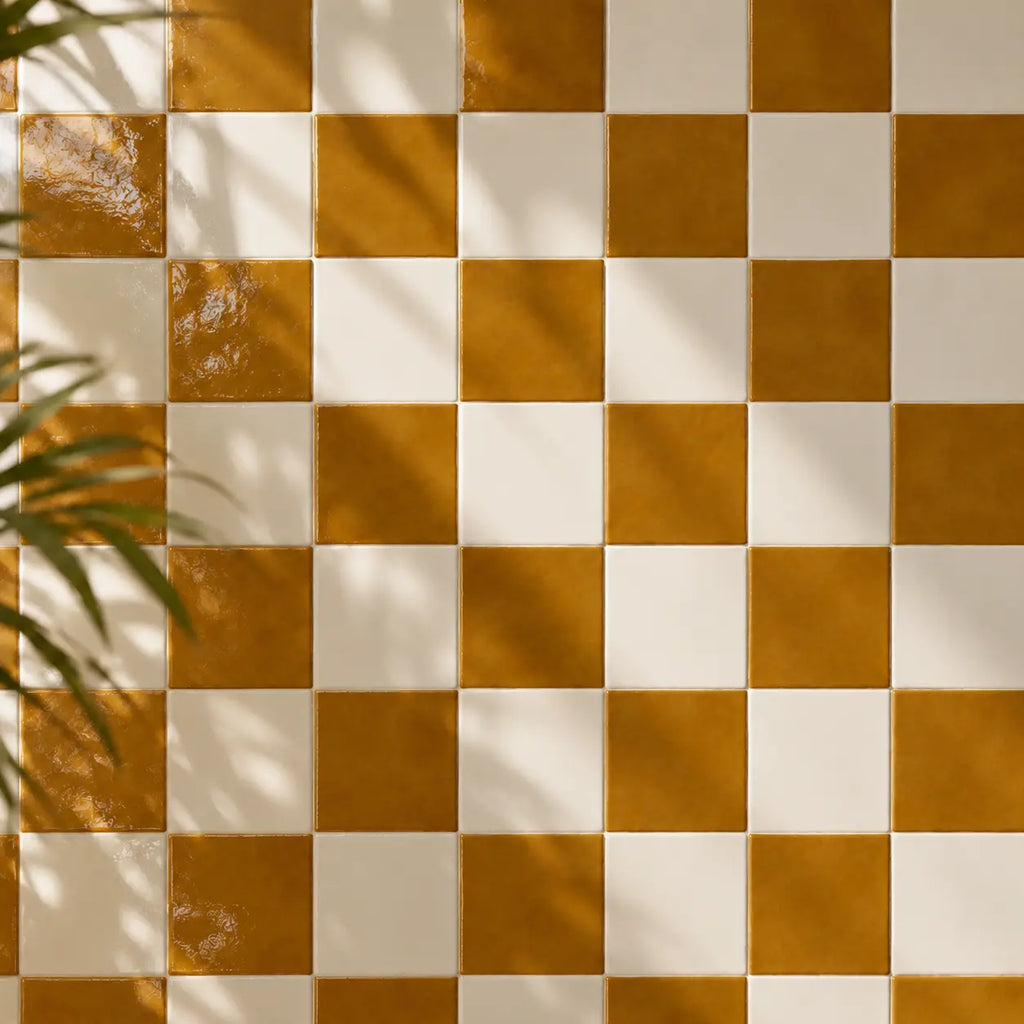 A checkered pattern of glossy amber light brown and off-white square tiles, with soft leaf shadows cast across the surface.