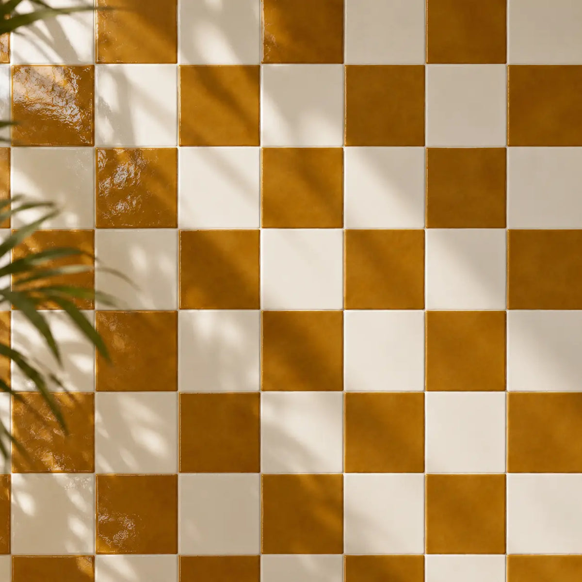 A checkered pattern of glossy amber light brown and off-white square tiles, with soft leaf shadows cast across the surface.