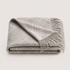 A folded gray woven throw blanket with fringed edges, shown on a plain light gray background.