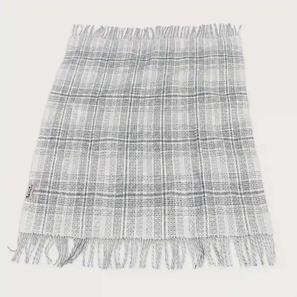 A fringed woven throw blanket with a gray and white plaid pattern, laid flat against a light off-white background.