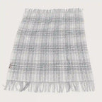 A fringed woven throw blanket with a gray and white plaid pattern, laid flat against a light off-white background.