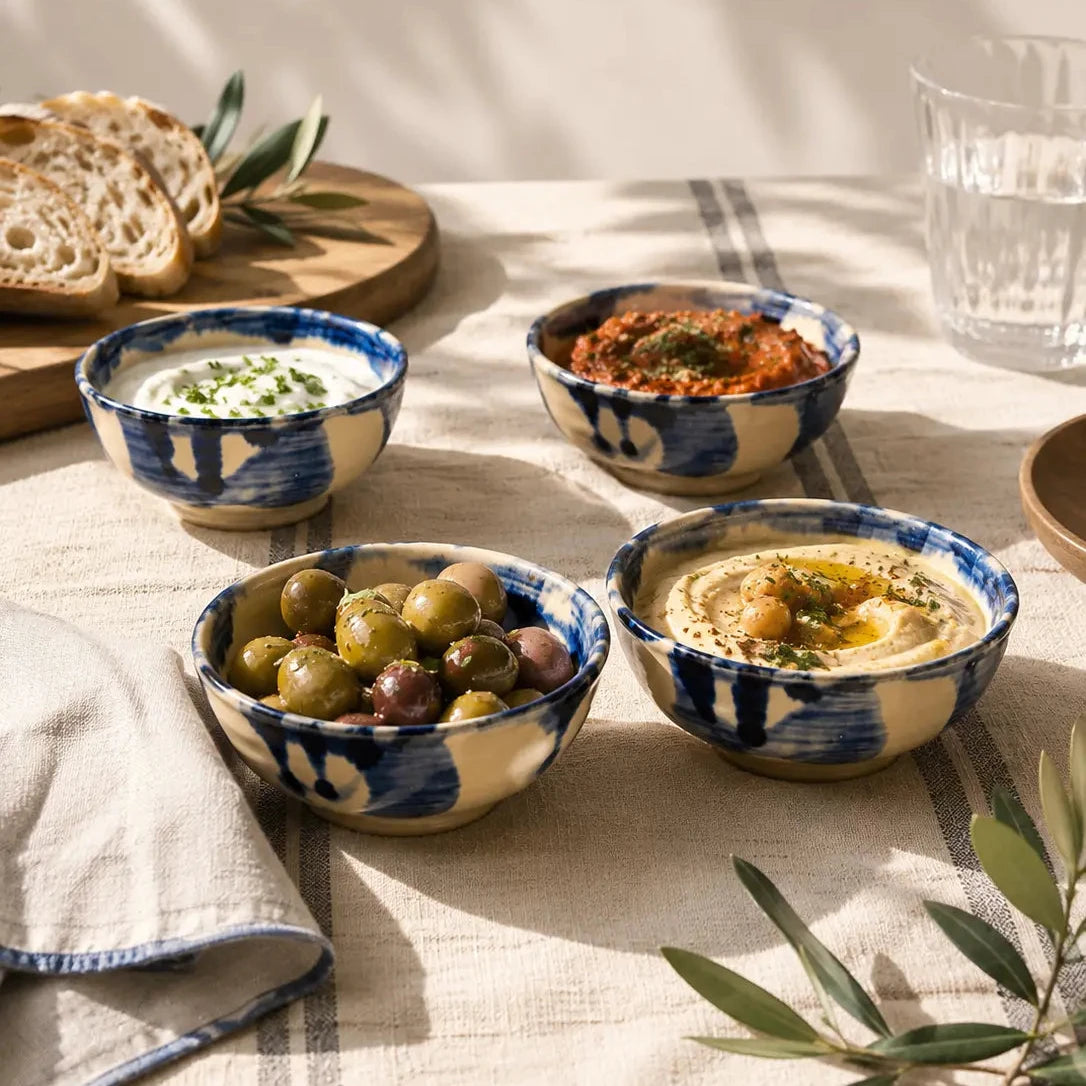 Assorted dips in blue and white bowls on a table with bread and olives.