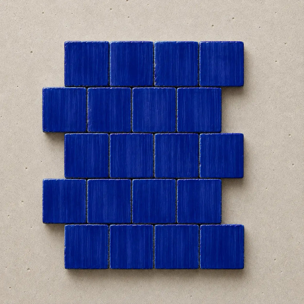 A set of small rectangular blue mosaic tiles arranged in a staggered brick pattern on a textured beige background.