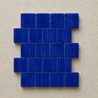 A set of small rectangular blue mosaic tiles arranged in a staggered brick pattern on a textured beige background.