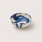 A small hand-painted ceramic snack bowl with a white base and blue brushstroke pattern, photographed on a light gray background.