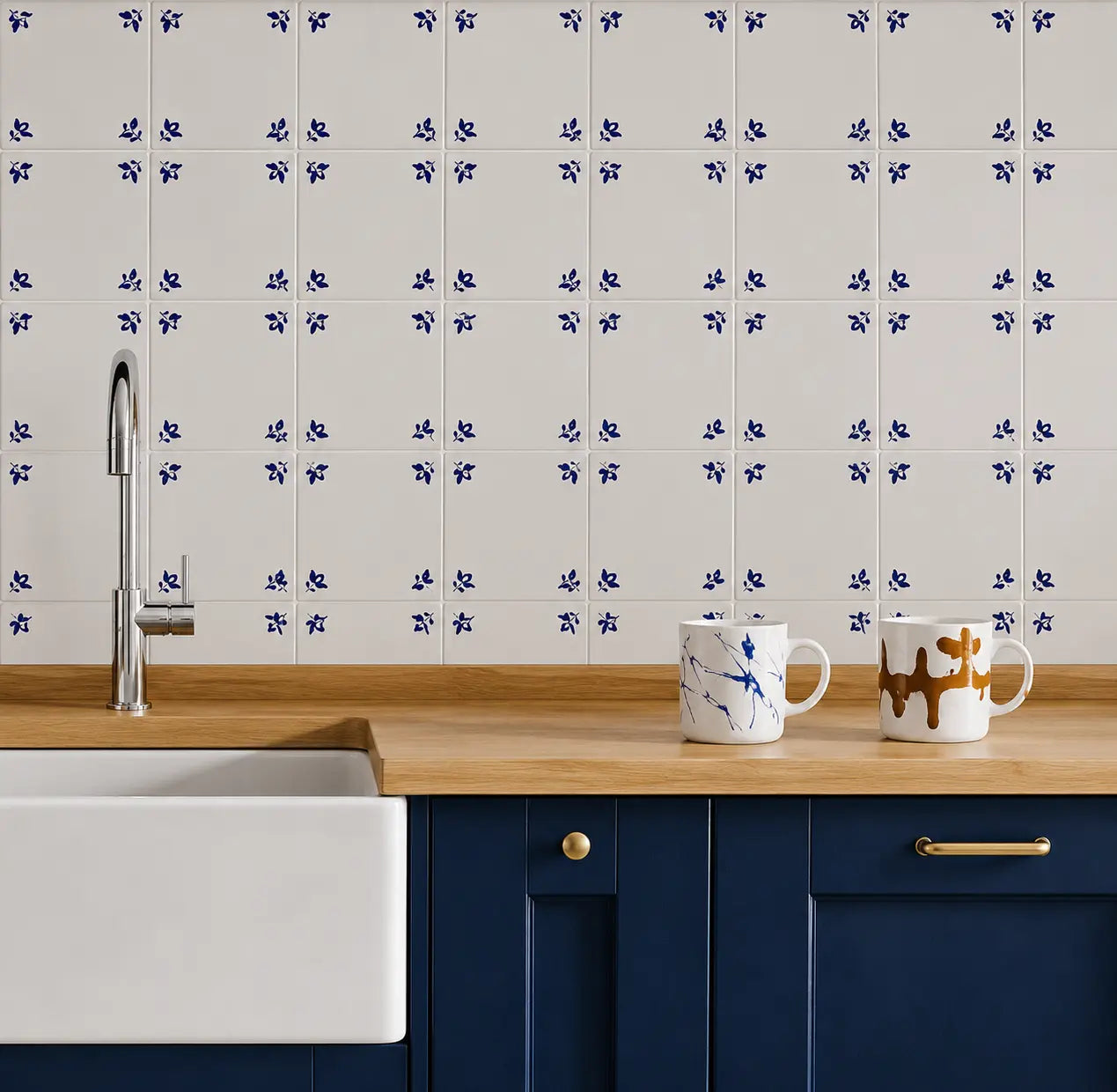 White ceramic kitchen wall tiles with a repeating blue floral pattern, installed above a wooden countertop with a white farmhouse sink, a chrome faucet, and two white mugs.