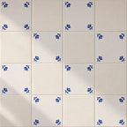 White ceramic tiles arranged in a grid, with several tiles decorated in the corners by small blue floral motifs.