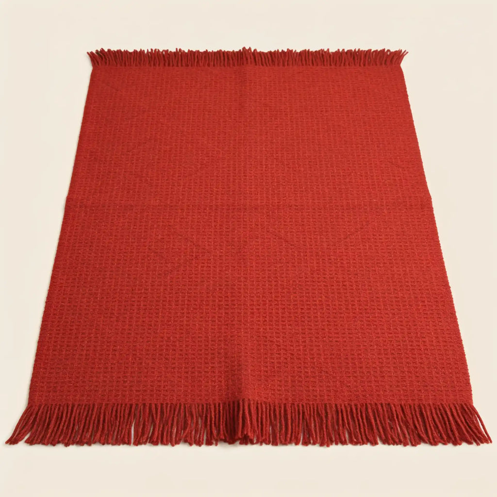 A red woven throw blanket with fringed edges, laid flat against a light cream background.