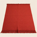 A red woven throw blanket with fringed edges, laid flat against a light cream background.