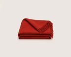 A folded red woven throw blanket with fringed edges, displayed on a clean white background.