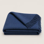 A folded navy blue textured wool throw blanket with fringed edges, displayed on a clean, light beige background.