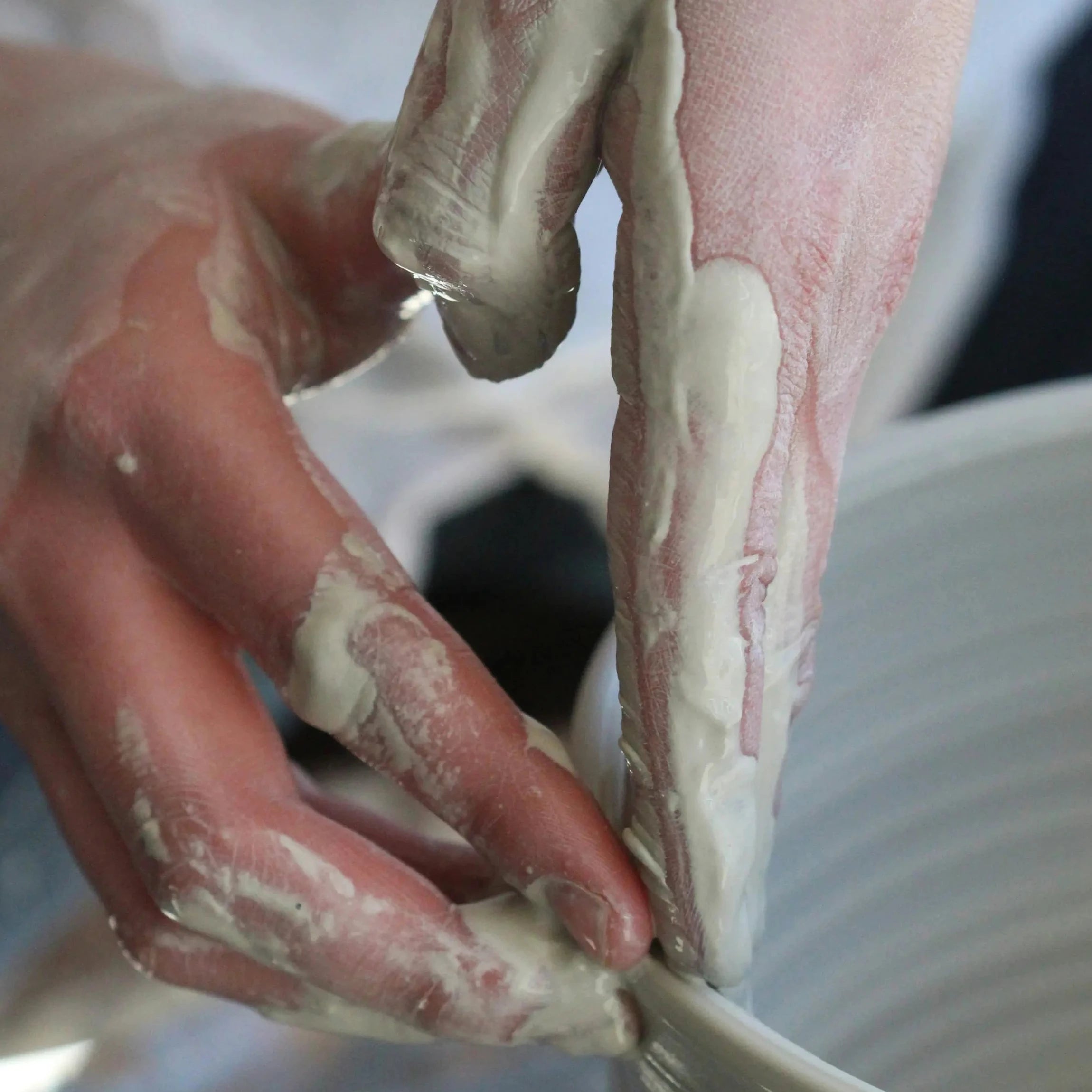 Close-up of hands applying a thick white clay or plaster slip to a white ceramic vessel.
