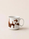 A white ceramic coffee mug with a brown dripping paint or chocolate splash design, set against a solid light beige background.