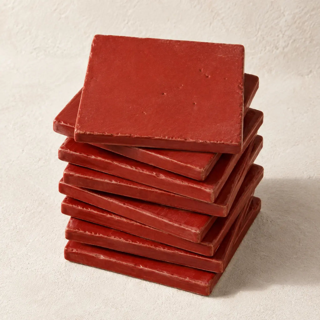 A stack of square red tiles or coasters with a matte, slightly textured surface, arranged on a light beige textured background.