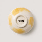 Ceramic snack bowl with yellow and white design on a light gray background, featuring the 'Cardoon Studio' logo.