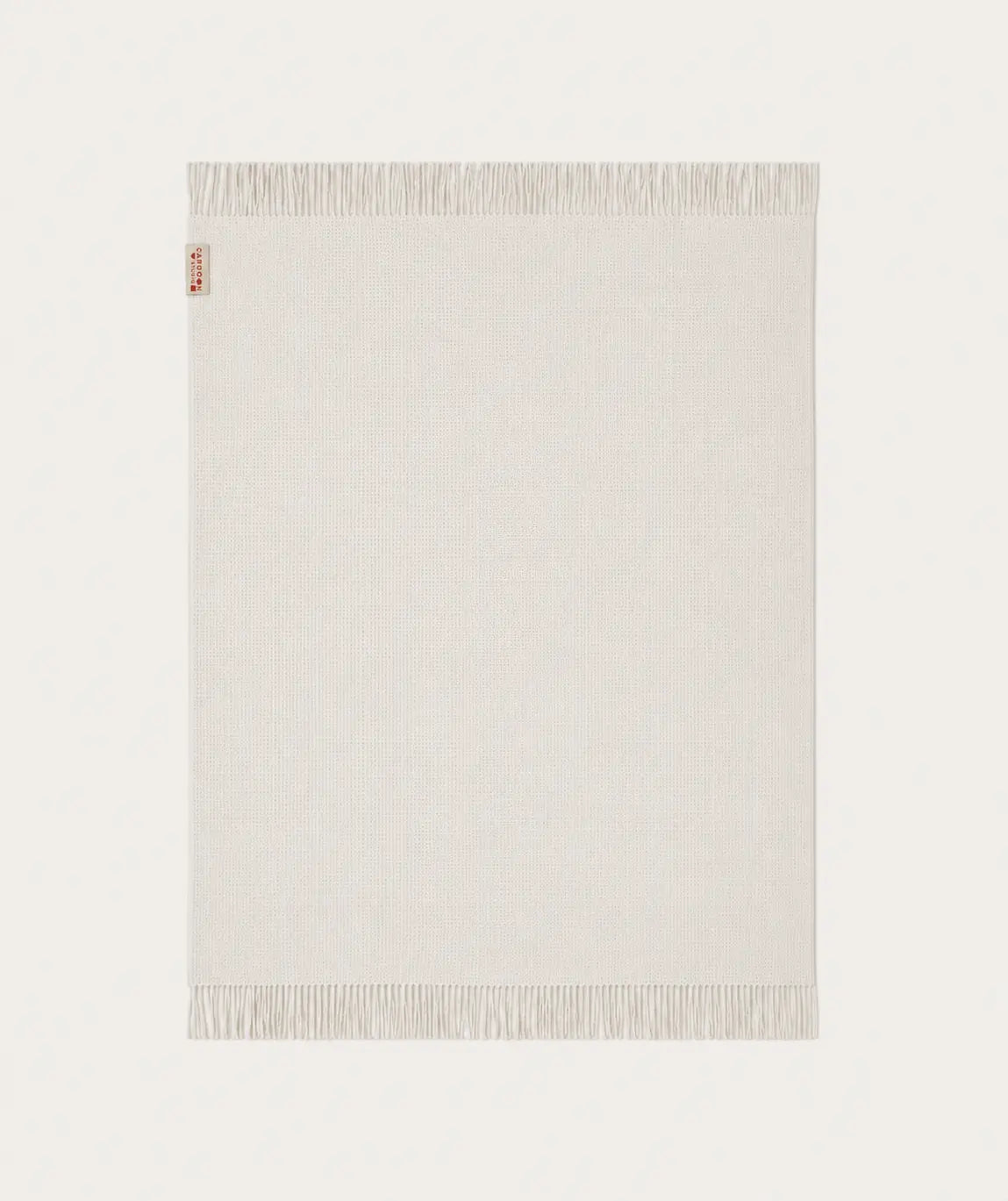 A light cream-coloured throw blanket with fringed edges, shown flat against a matching off-white background. A small red and white tag is visible on the top-left corner.