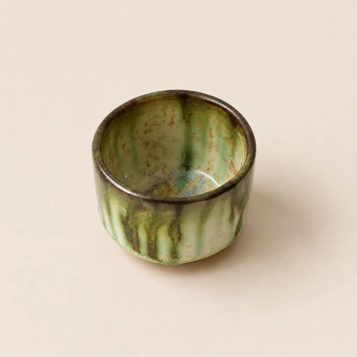 A small glazed ceramic matcha bowls with a vertical drip design in green and black against a solid beige background.