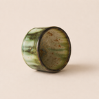 A small glazed ceramic matcha bowls with a vertical drip design in green and black against a solid beige background.