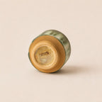 A small ceramic matcha bowl shown from its base, featuring a glossy green glaze and a natural tan clay foot, photographed on a solid light beige background.