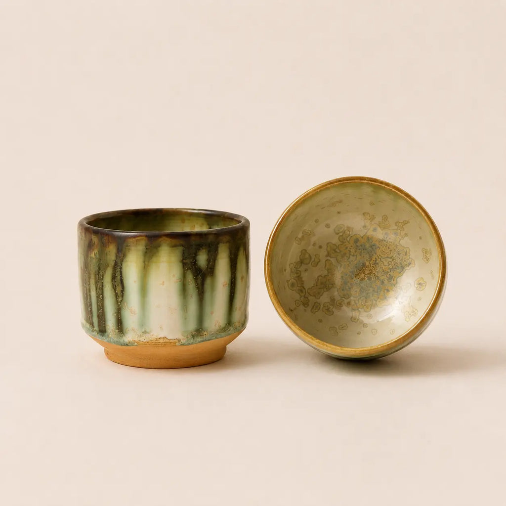 A ceramic matcha bowl shown from two angles, one facing forward to reveal a green and brown glaze with a tan base, and the other turned sideways to show the textured, speckled interior with a gold-toned rim, set against a solid beige background.
