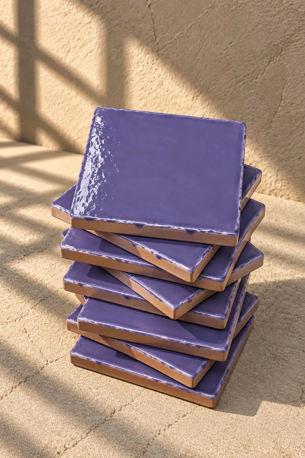 A stack of square ceramic lilac tiles in a muted lavender-purple glaze, with one coaster resting on top, set against a textured beige background.