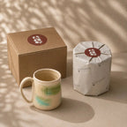 Porcelain mug with a cardboard box and white bag featuring a logo on a beige background
