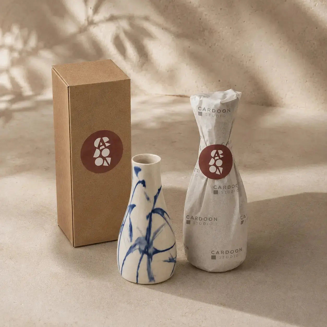 Two ceramic vases and a cardboard box with a brand logo on a beige background