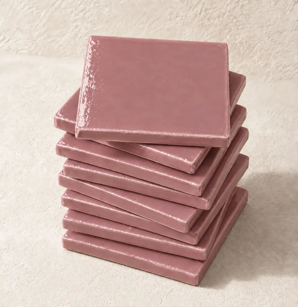 A stack of square dusty pink ceramic tiles on a textured beige surface.