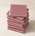 A stack of square dusty pink ceramic tiles on a textured beige surface.