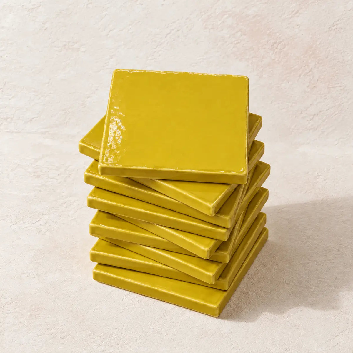 A stack of glossy square citron yellow coasters on a textured off-white background.