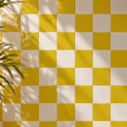 Citron yellow and white checkered tiled wall with soft leaf shadows cast across it.