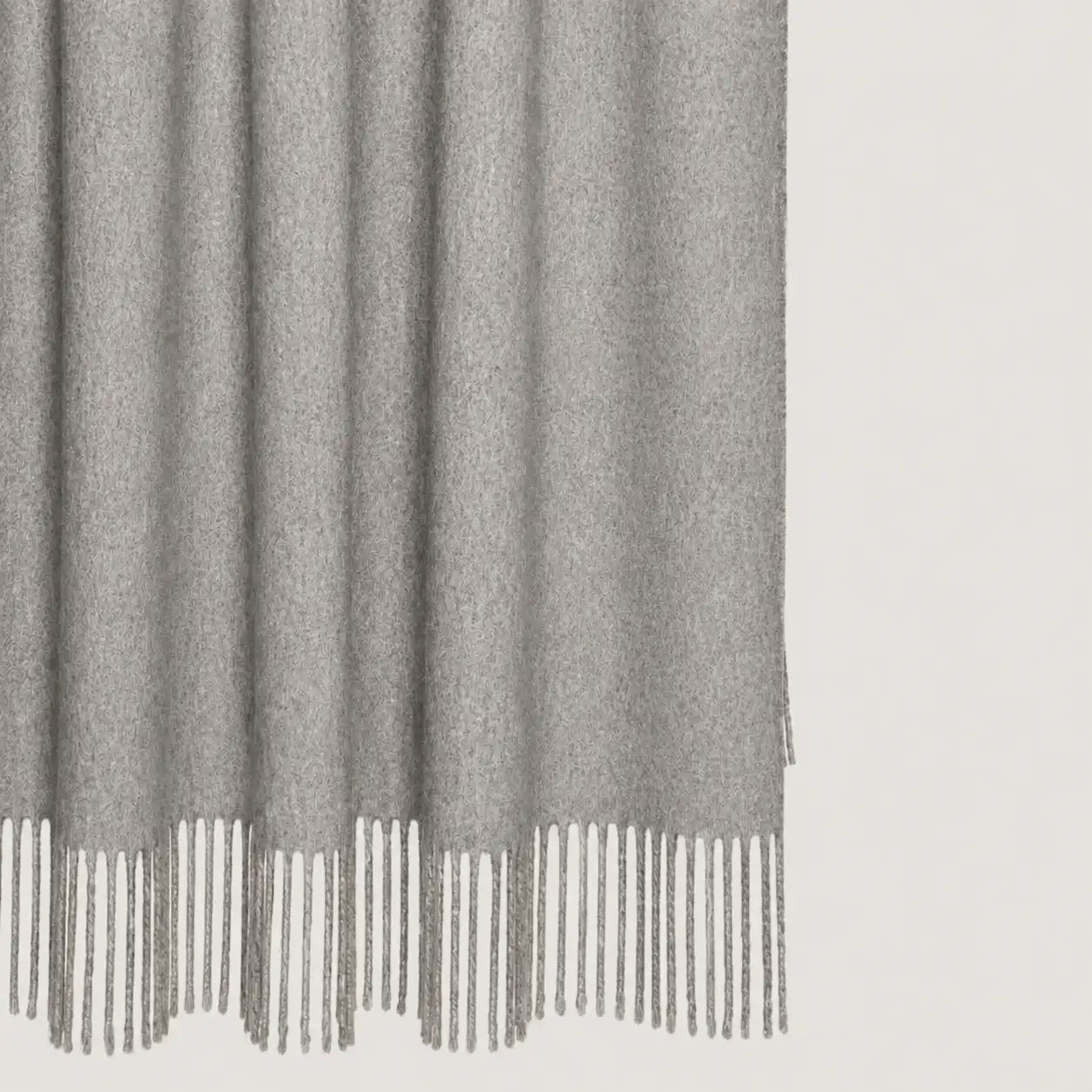 A close-up of a light gray textured throw blanket throw with fringe detailing along the bottom edge, shown against a plain off-white background.
