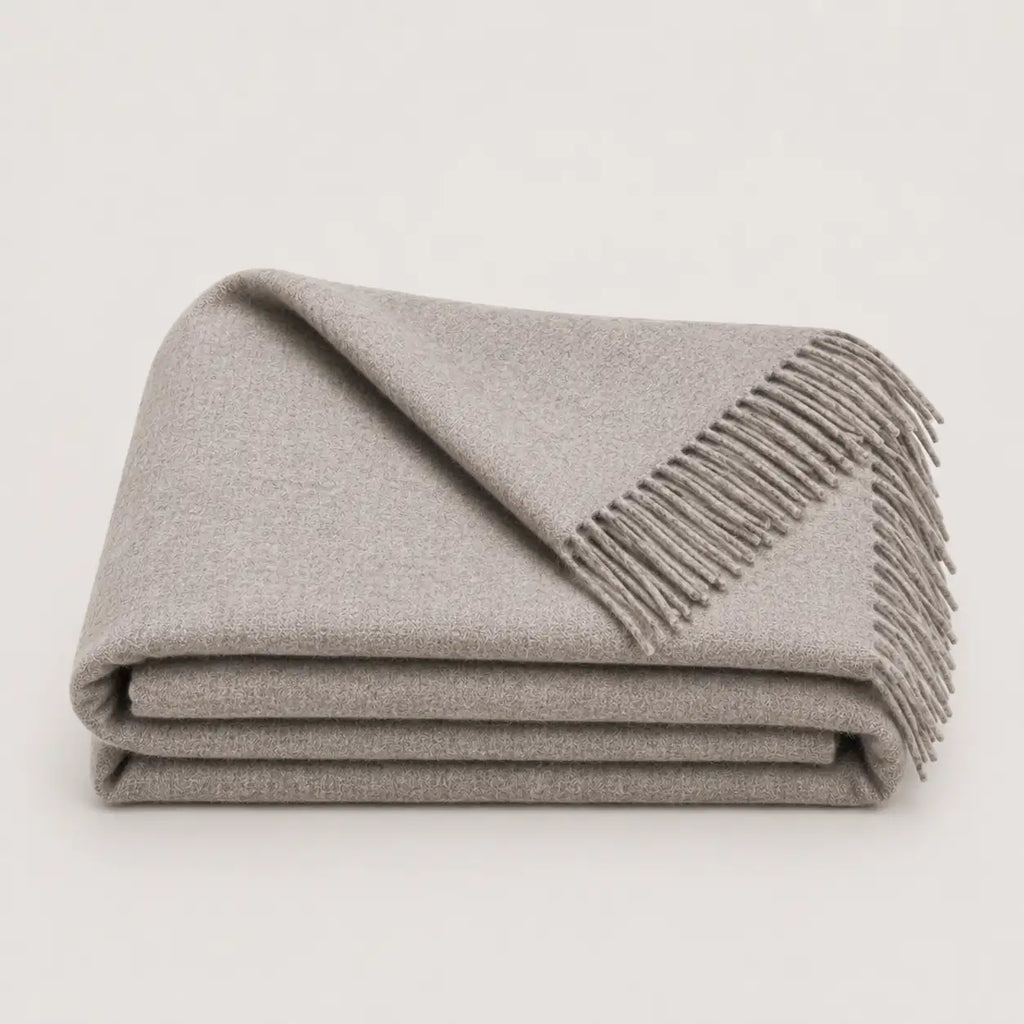 A folded light gray woven alpaca throw blanket with fringed edges, photographed on a clean off-white background.