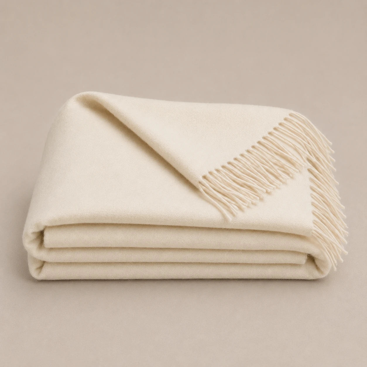 A folded cream-colored alpaca throw blanket with fringed edges, displayed on a neutral beige background.