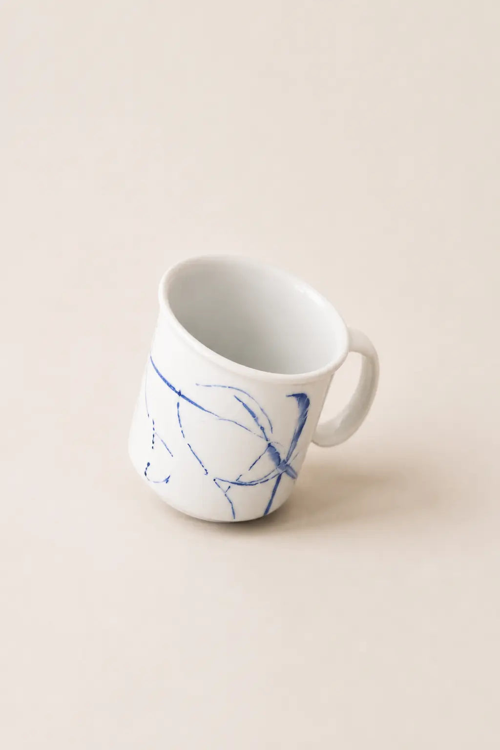 A white ceramic mug with a blue abstract line pattern, photographed on a solid, warm off-white background.