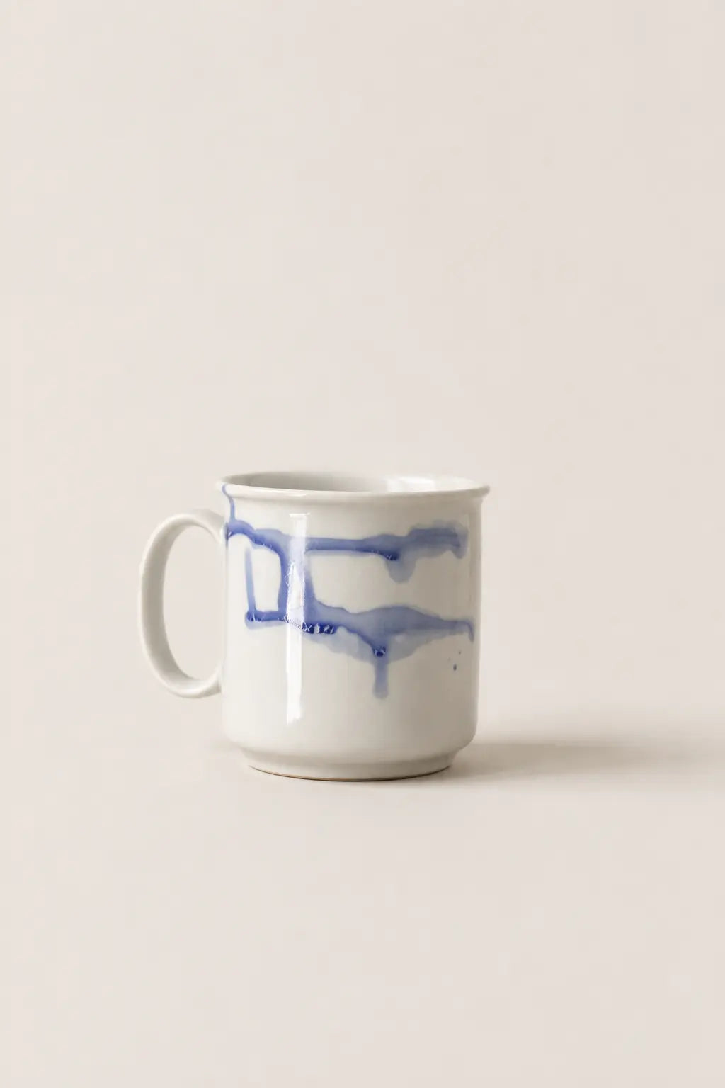 A white ceramic mug with a blue watercolor-style abstract stripe pattern, set against a solid, warm off-white background.