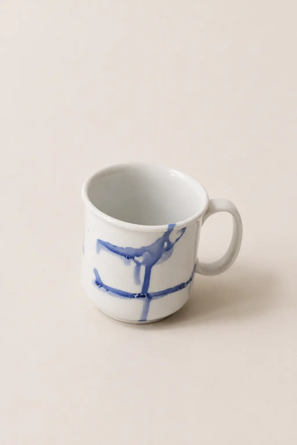 A white ceramic mug with a blue abstract painted design, set against a solid beige background.